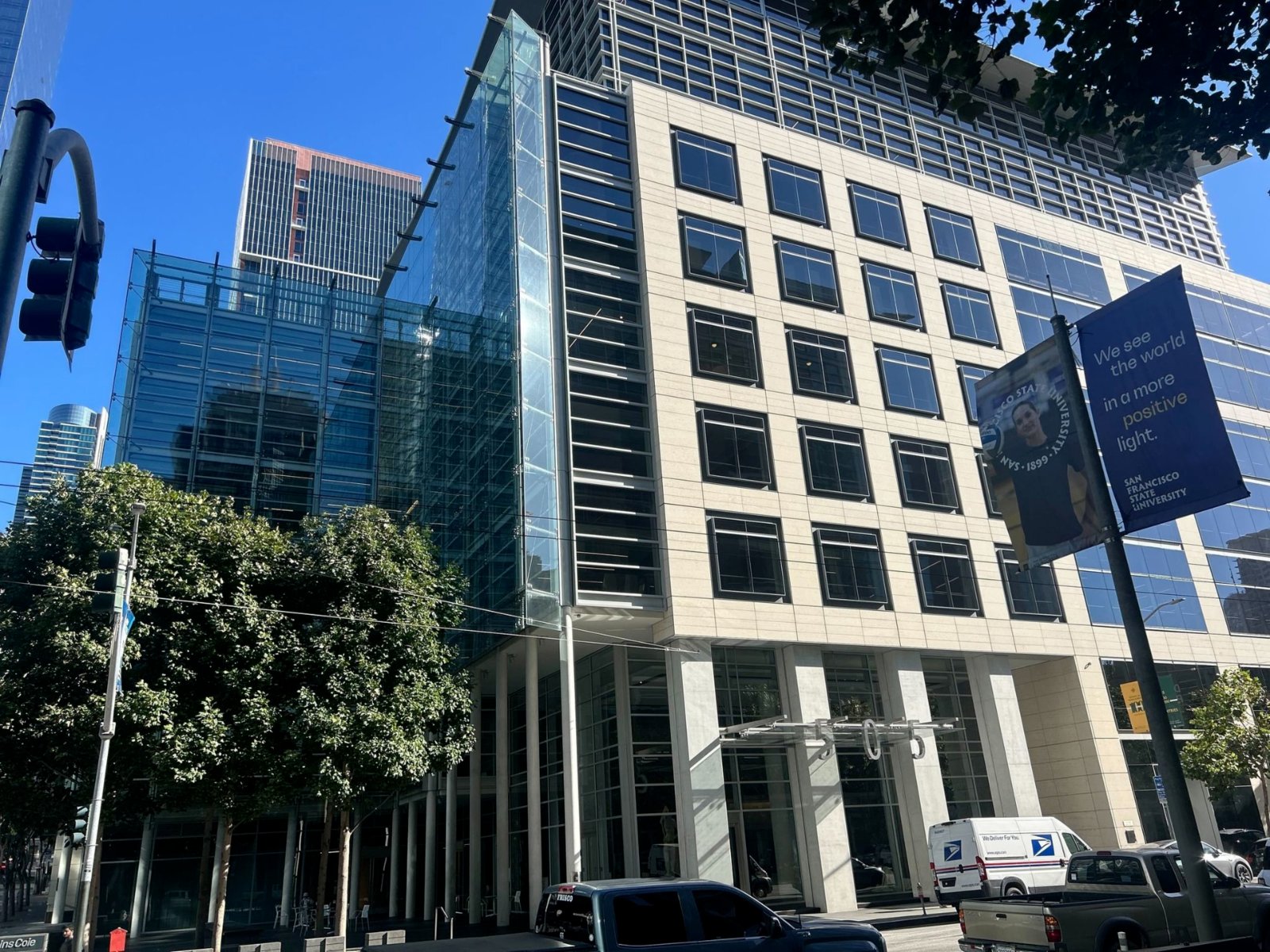 A glass-and-stone office tower in downtown San Francisco under a clear blue sky, seen from street level.
